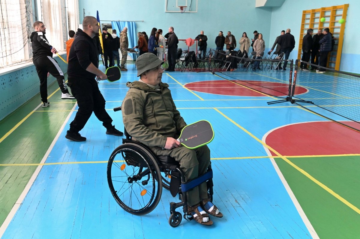 Ukrainian veteran in a wheelchair holds a pickleball paddle during an indoor match.